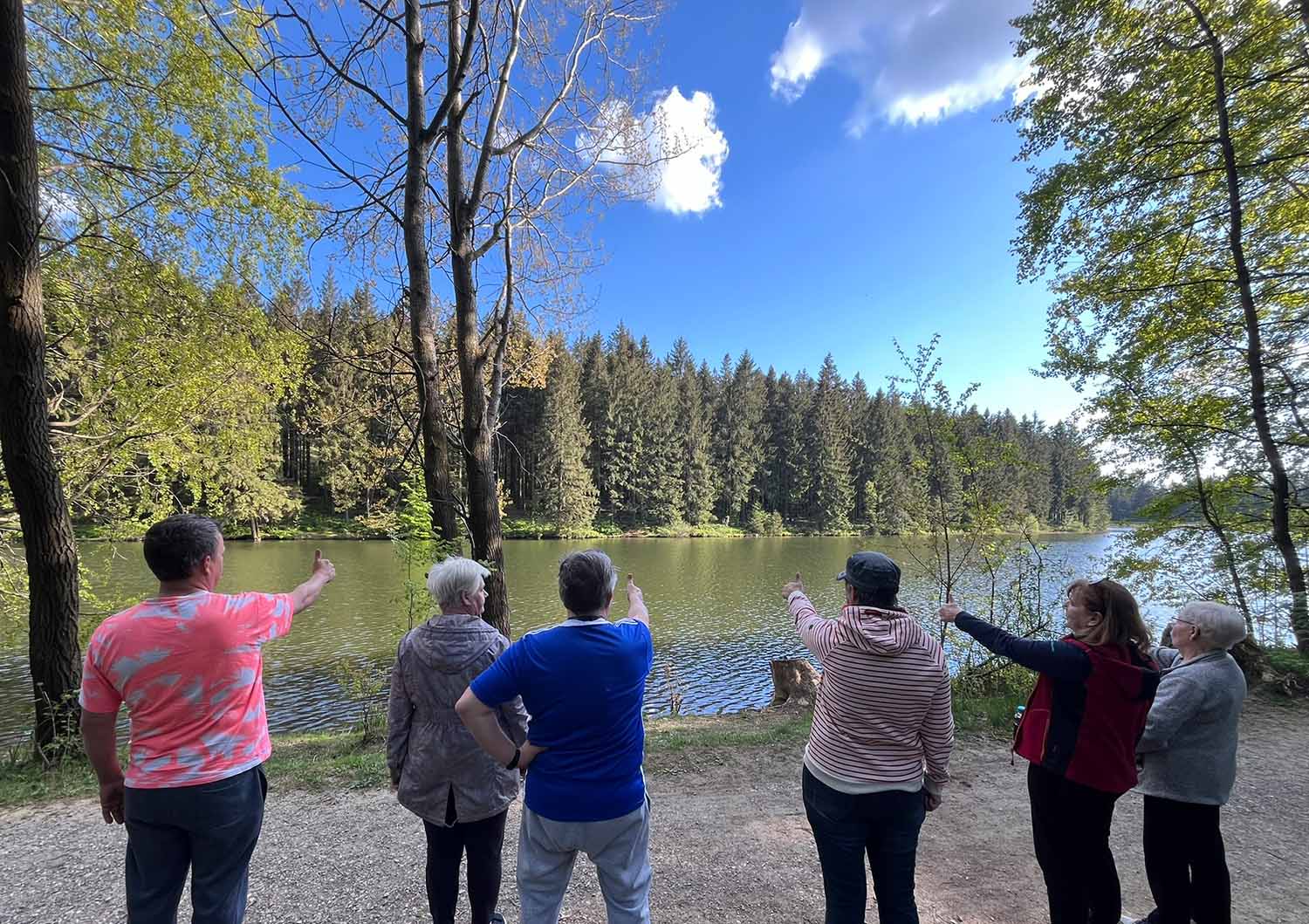 Eine Gruppe schaut über eine See in den gegenüberliegeden Wald